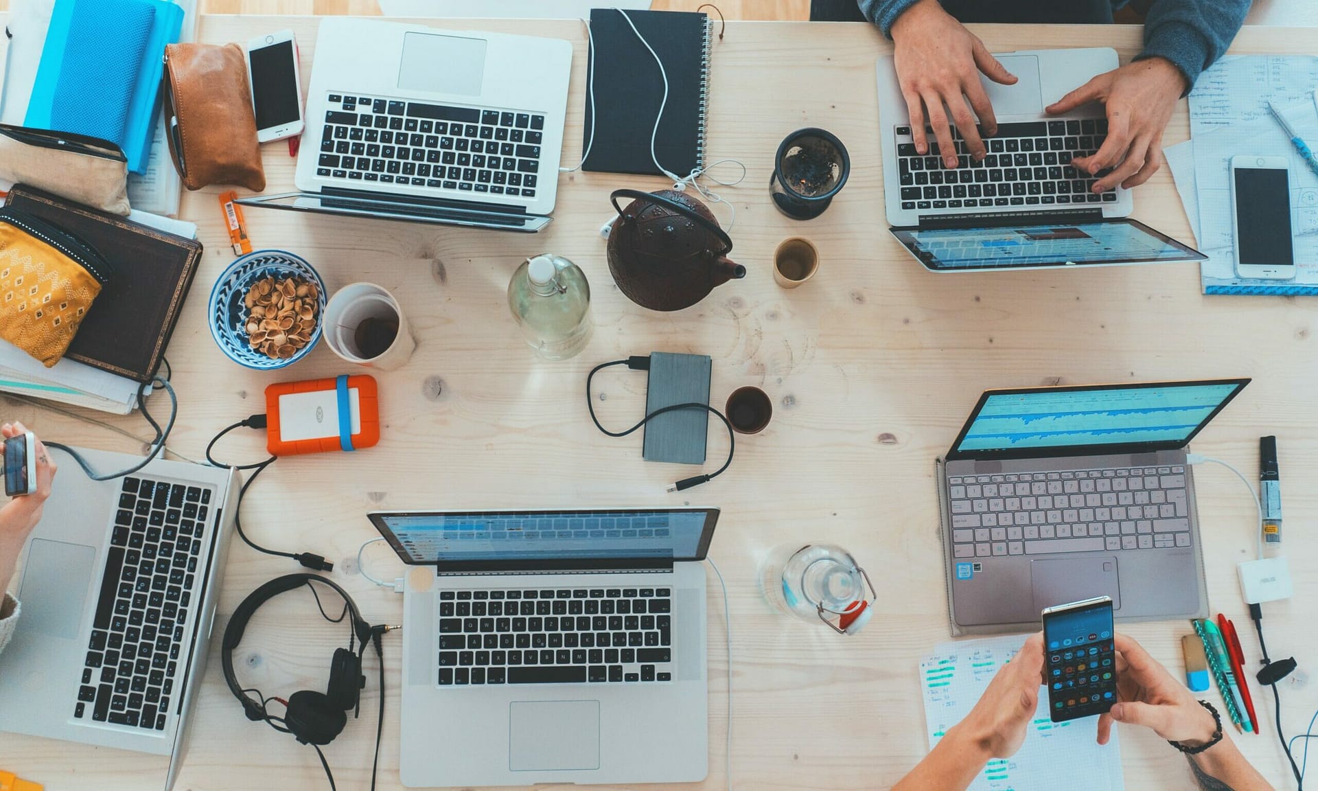 L'image d'un bureau avec plusieurs personnes qui travaillent devant des ordinateurs. On peut voir des stylos, des carnets, un casque et des tasses.